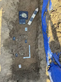 Archeologický výkop s označenými artefakty a měřícím pravítkem v zemině