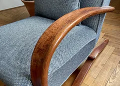 Detail křesla s dřevěnou područkou a modrým čalouněním na dřevěné podlaze.
