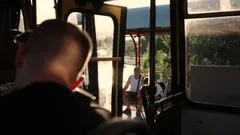 Muž sedí na venkovské autobusové zastávce za teplého večerního světla