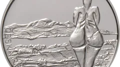 Stříbrná mince s reliéfem postavy a krajinou, umělecký design, detailní ražba.