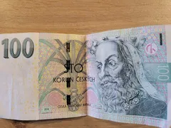 Česká bankovka 100 korun s portrétem Karla IV. položená na dřevěném stole.
